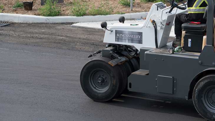 A construction worker driving a paving vehicle on a newly paved parking lot.