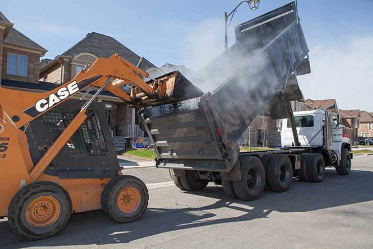 A paving vehicle scooping loose asphalt out of the back of a large dump truck.