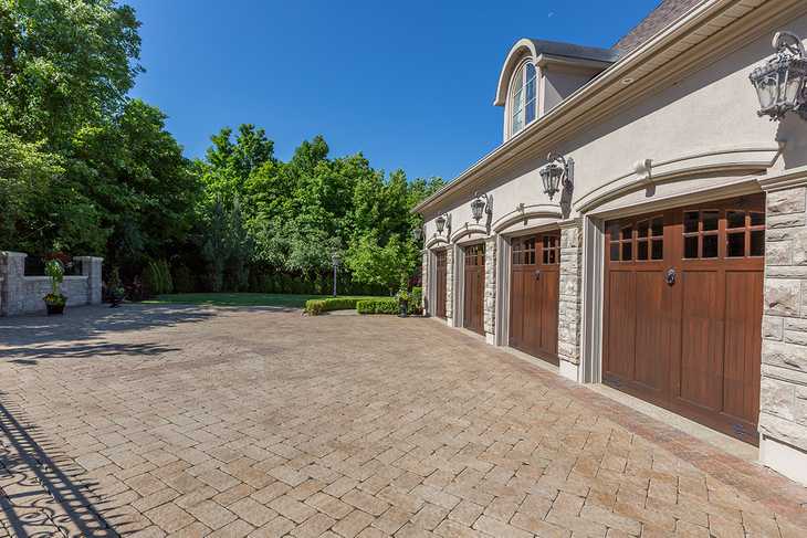 A large cobblestone driveway in front of a large home's three garage doors.
